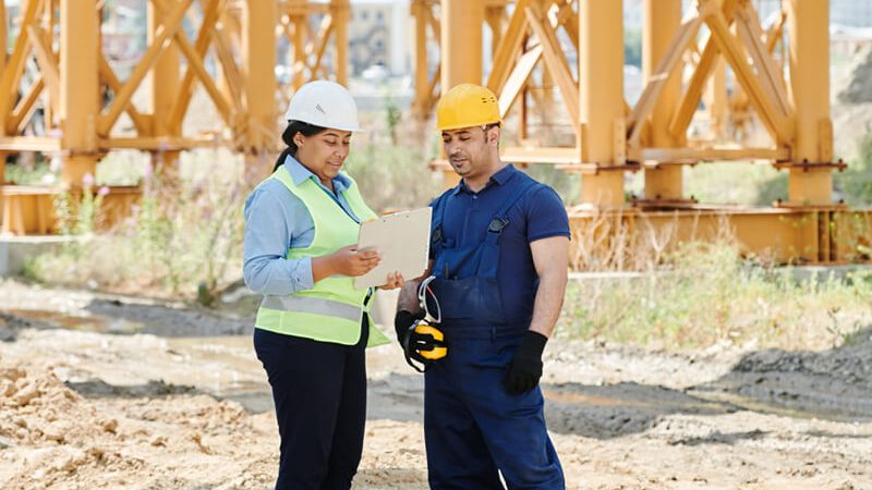 Bauleiterin und Handwerker stimmen sich mit Checkliste auf der Baustelle ab