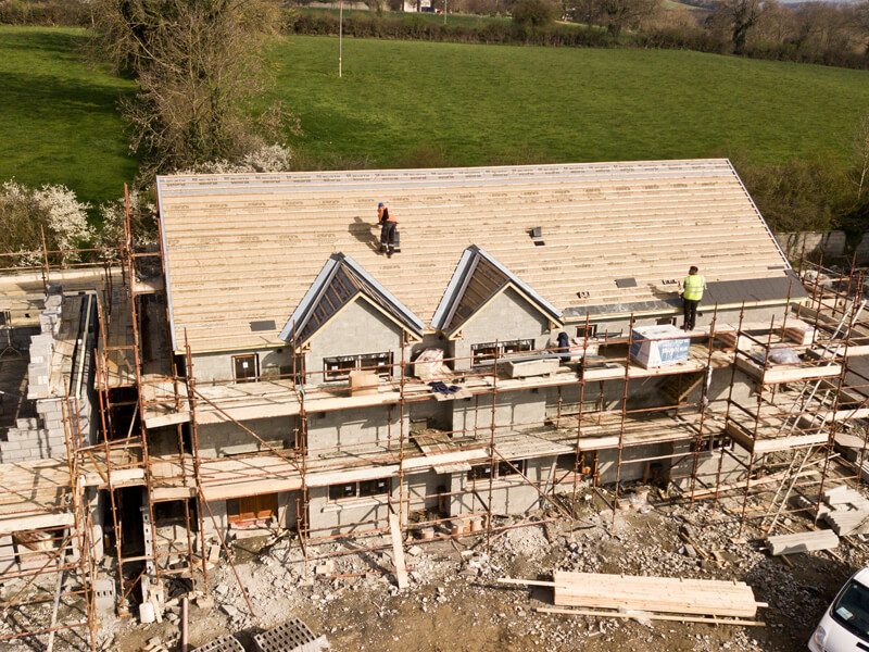 Neubau eines Einfamilienhauses: eingerüstetes Mauerwerk, Handwerker auf dem Dachstuhl